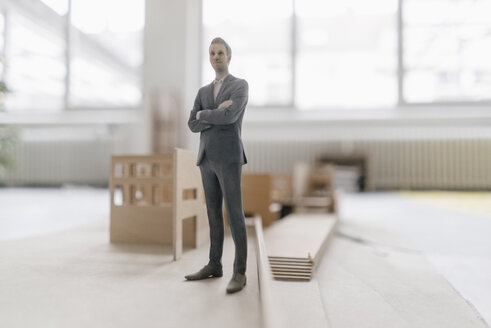 Miniature businessman figurine standing at architectural model - FLAF00116