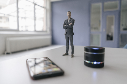 Miniature businessman figurine standing next to smart home loudspeaker and smartphone stock photo