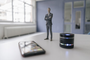 Miniatur-Geschäftsmann-Figur neben Smart-Home-Lautsprecher und Smartphone - FLAF00126