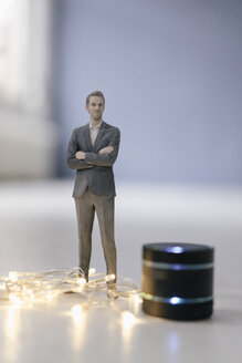 Miniature businessman figurine standing next to smart home loudspeaker with chain of lights - FLAF00130