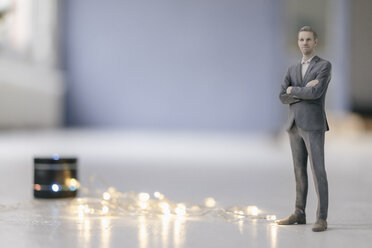 Miniature businessman figurine standing next to smart home loudspeaker with chain of lights - FLAF00131