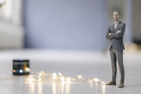 Miniatur-Geschäftsmann-Figur neben einem Smart-Home-Lautsprecher mit Lichterkette - FLAF00131