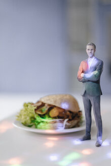 Miniatur-Geschäftsmann-Figur, die neben Fast Food steht und von Lichtpunkten umgeben ist - FLAF00139