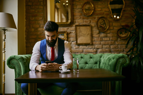 Fashionable young man sitting on couch in a cafe using cell phone stock photo
