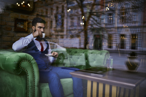 Fashionable young man sitting on couch in a cafe drinking coffee stock photo