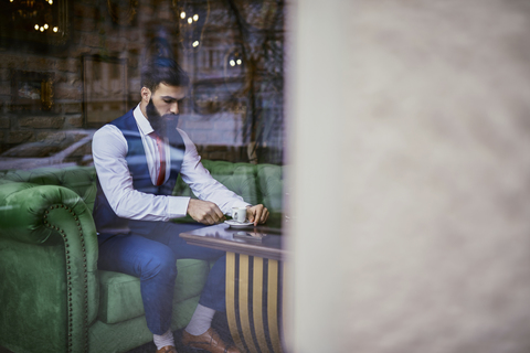 Modischer junger Mann sitzt auf einer Couch in einem Café, lizenzfreies Stockfoto