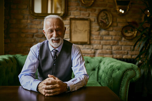 Porträt eines eleganten älteren Mannes, der lächelnd auf einer Couch in einem Café sitzt - ZEDF01104