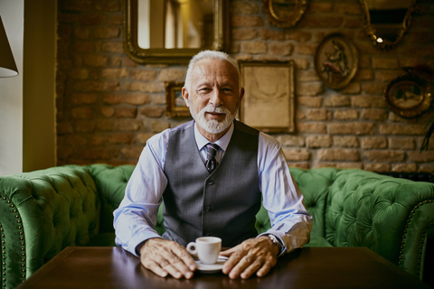 Porträt eines eleganten älteren Mannes, der auf einer Couch in einem Café sitzt, lizenzfreies Stockfoto