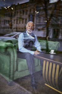 Eleganter älterer Mann sitzt auf einer Couch in einem Café und schaut aus dem Fenster - ZEDF01110