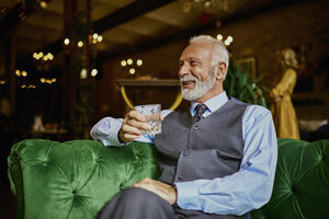 Porträt eines eleganten älteren Mannes, der auf einer Couch in einer Bar sitzt und einen Becher hält - ZEDF01120