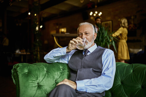 Porträt eines eleganten älteren Mannes, der auf einer Couch in einer Bar sitzt und aus einem Becher trinkt - ZEDF01121