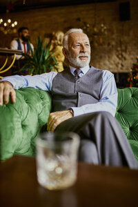 Porträt eines eleganten älteren Mannes, der auf einer Couch in einer Bar sitzt - ZEDF01124