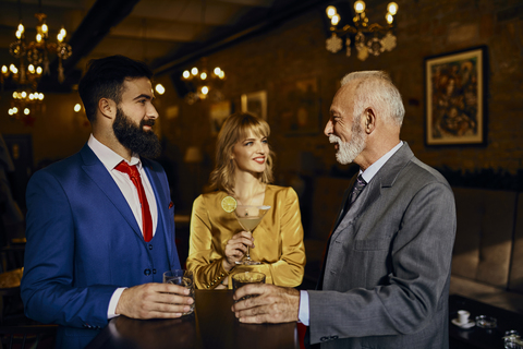 Zwei elegante Männer und eine Frau unterhalten sich in einer Bar, lizenzfreies Stockfoto