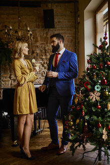 Elegant couple with drinks standing at Christmas tree - ZEDF01148