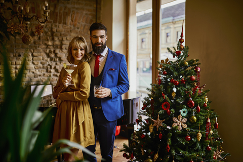 Porträt eines eleganten Paares mit Getränken am Weihnachtsbaum, lizenzfreies Stockfoto