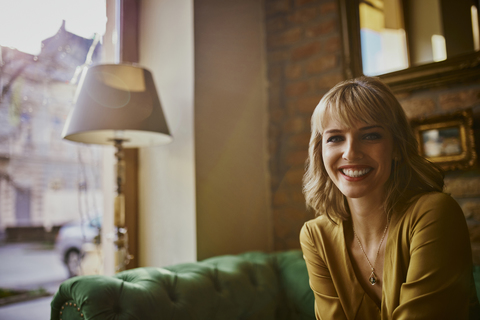 Porträt einer lächelnden eleganten Frau, die auf einer Couch sitzt, lizenzfreies Stockfoto