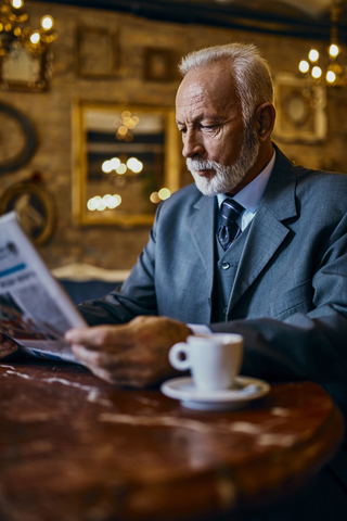 Elegant senior man reading newspaper in a cafe stock photo