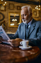 Elegant senior man reading newspaper in a cafe - ZEDF01177