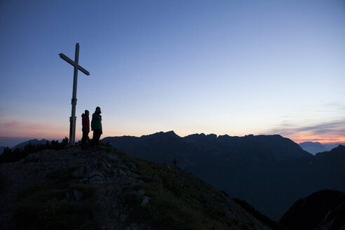 Österreich, Tirol, zwei Wanderer stehen am Gipfelkreuz - FAF00077