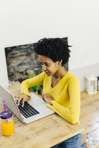 Junge Frau sitzt am Schreibtisch und benutzt einen Laptop, lizenzfreies Stockfoto