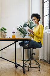 Young woman sitting at home reading on digital tablet - GIOF03806