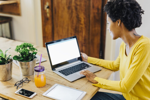 Young woman sitting at table with several portable device - GIOF03808