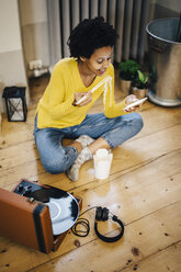 Junge Frau sitzt zu Hause auf einem Plattenspieler und überprüft ihr Smartphone, während sie Nudeln isst - GIOF03822
