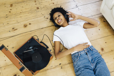 Young woman at home listening vinyl records, lying on ground - GIOF03827