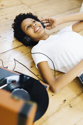 Young woman at home listening vinyl records, lying on ground - GIOF03828
