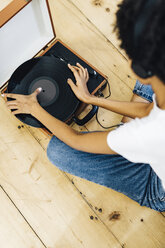 Young woman sitting on grounf listening music from record player - GIOF03830