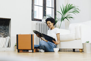 Young woman sitting on grounf listening music from record player - GIOF03835