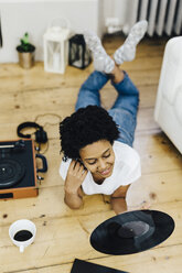 Young woman at home listening vinyl records, lying on ground - GIOF03839