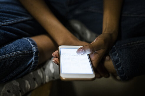 Junge Frau, die nachts zu Hause sitzt und ein beleuchtetes Smartphone in der Hand hält - GIOF03844