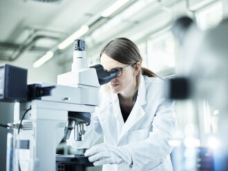 Laboratory technician looking through microscope in lab - CVF00037