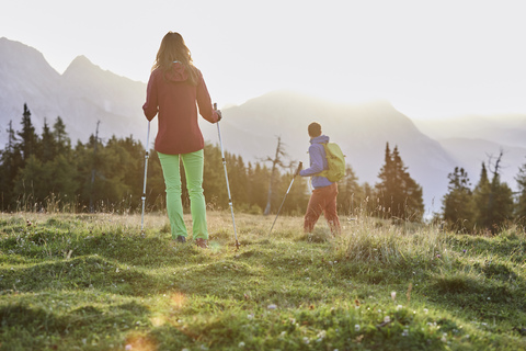 Österreich, Tirol, Mieminger Plateau, zwei Wanderer auf Almwiese bei Sonnenaufgang, lizenzfreies Stockfoto