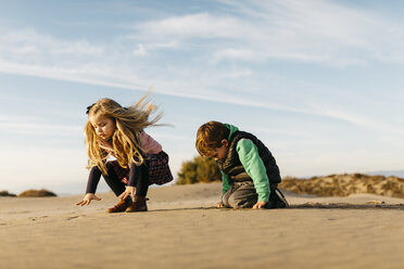 Two children playing with the sand on the beach in winter - JRFF01528