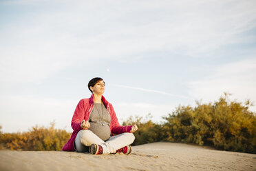 Pregnant woman practicing yoga on the beach in winter - JRFF01534