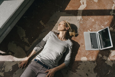 Frau schläft auf dem Boden neben dem Laptop - KNSF03550