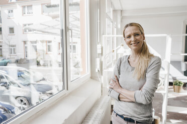 Porträt einer lächelnden Frau, die am Fenster steht - KNSF03551