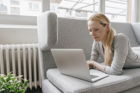 Frau auf Couch liegend mit Laptop, lizenzfreies Stockfoto