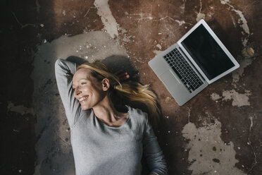 Smiling woman lying on the floor next to laptop - KNSF03554