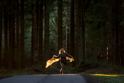Young woman holding blanket running on country road through forest stock photo