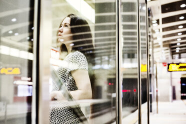 Porträt einer jungen Frau, die hinter einer Glaswand auf dem Bahnsteig einer U-Bahn-Station wartet - JATF00997