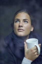 Portrait of young woman with coffee mug looking out of window - PNEF00397