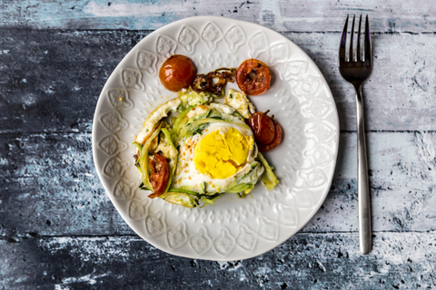 Nudelnest mit Ei, Zucchini-Nudeln mit Ei, Tomate und roter Zwiebel, lizenzfreies Stockfoto