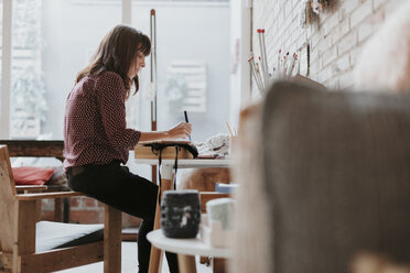 Frau sitzt im Studio und macht Notizen - OCAF00028