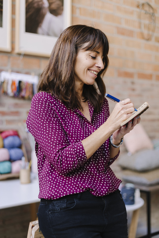 Lächelnde Frau im Strickstudio, die sich Notizen macht, lizenzfreies Stockfoto