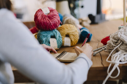 Nahaufnahme einer Frau, die auf einem Tisch mit Strickzeug Notizen macht - OCAF00040