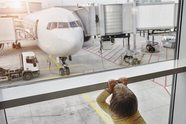 Kleines Mädchen schaut durch das Fenster auf ein Flugzeug auf dem Vorfeld - RORF01058