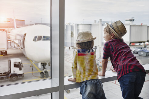 Zwei Kinder mit Strohhüten schauen durch ein Fenster auf ein Flugzeug auf dem Vorfeld - RORF01059